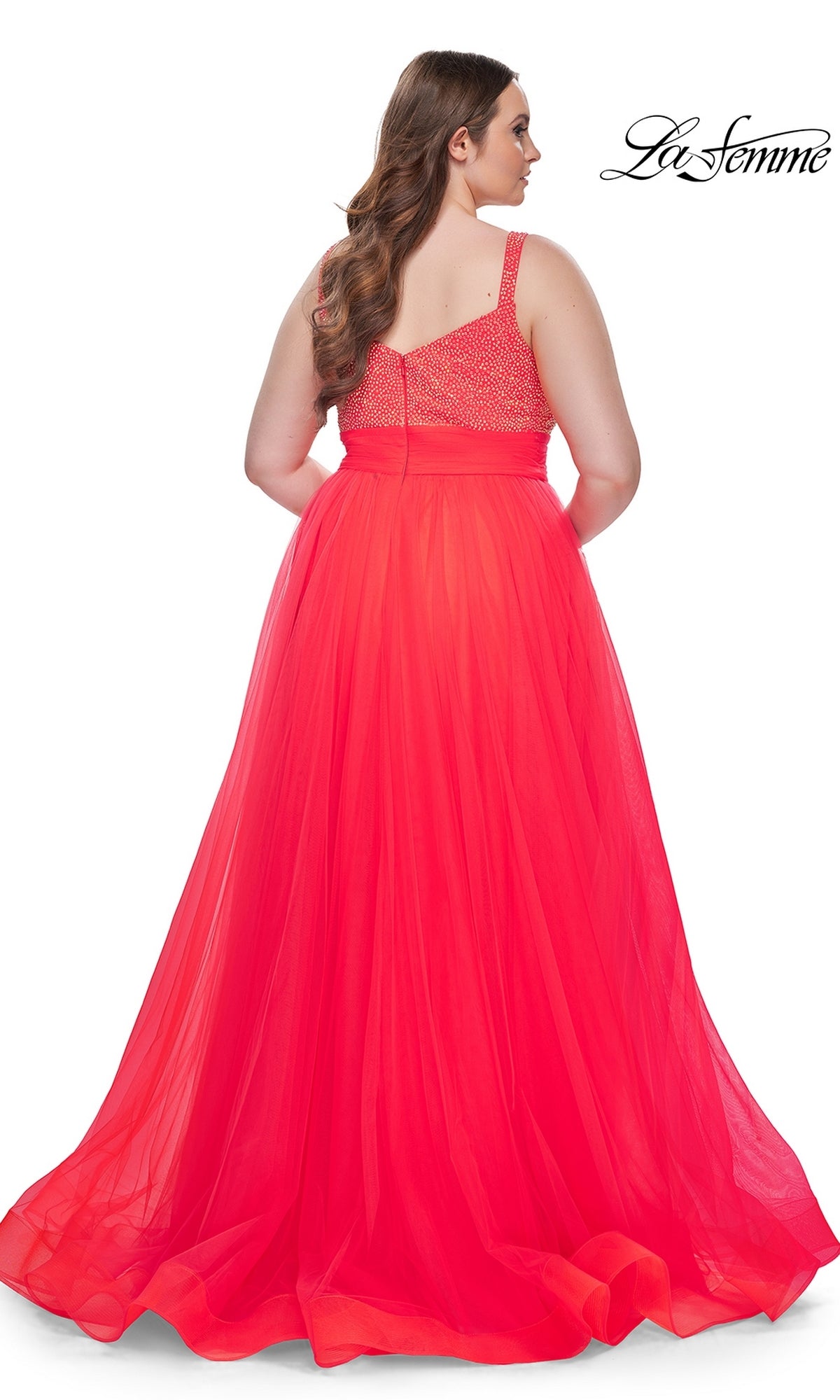 A woman with long brown hair is shown from the back wearing the La Femme Long Prom Dress 31251, a plus-size gown with a beaded bodice and flowing tulle skirt.